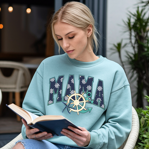 Woman wearing Chambray Mama Nautical sweatshirt with coastal ship wheel artwork while reading outdoors.