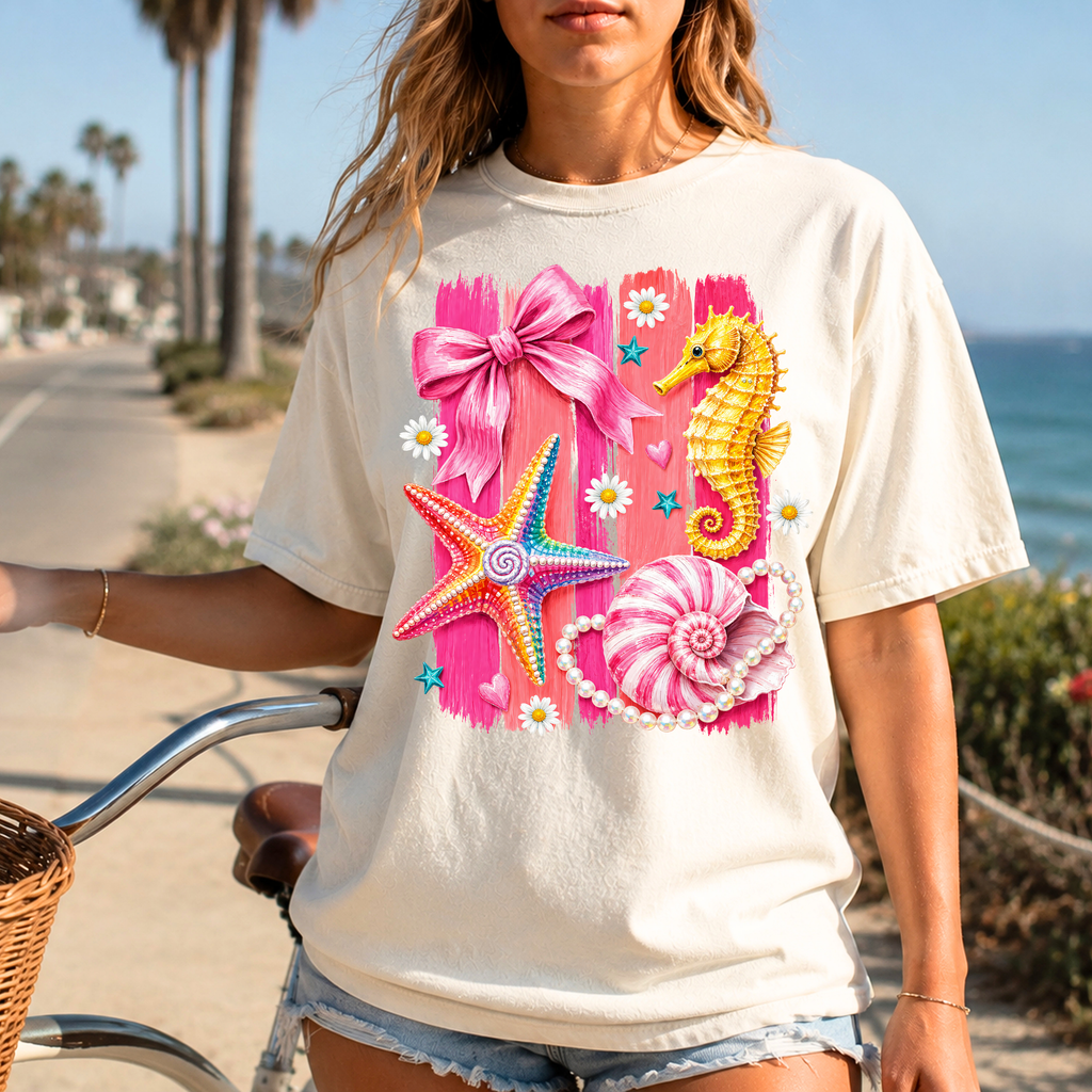 Ivory coastal graphic tee with pink seahorse, starfish, seashell, and bow artwork perfect for beach vacations and summer outfits.