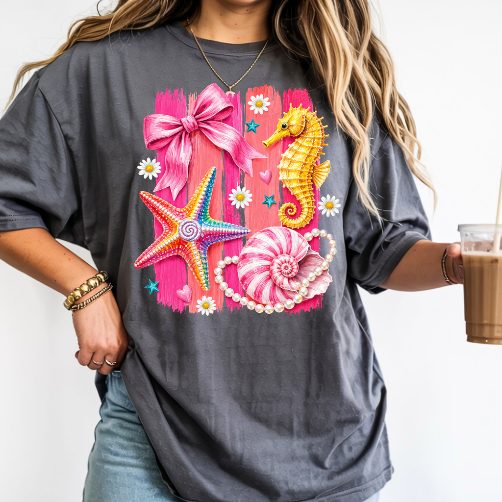 Pepper colored coastal graphic tee with pink beach aesthetic design featuring a seahorse, starfish, bow, pearls, and seashells.