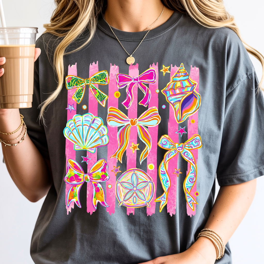 Woman wearing pepper color coastal graphic tee featuring colorful seashells ribbons and beach inspired artwork