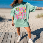 Woman wearing bay green coastal graphic tee with seashell and ribbon beach design on boardwalk
