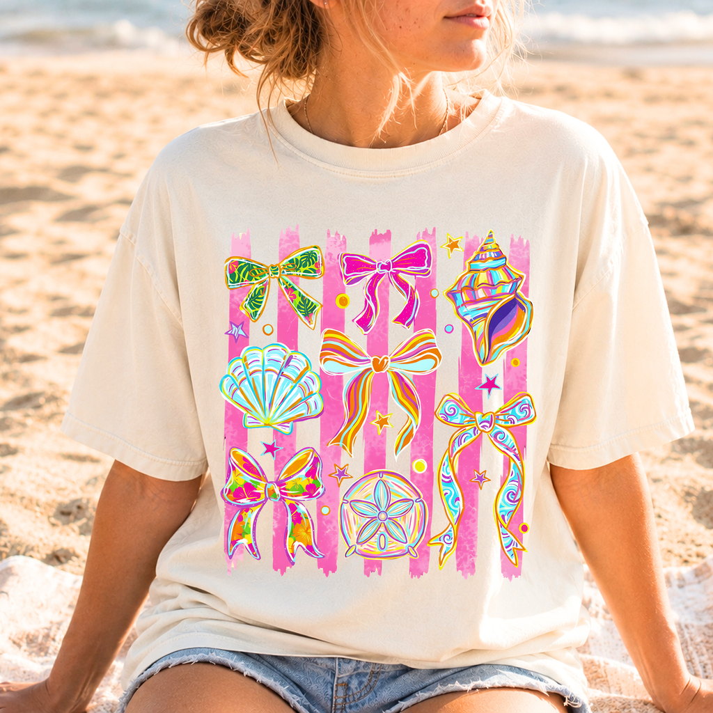 Woman wearing ivory Seashells and Ribbons graphic tee featuring colorful seashells and bows